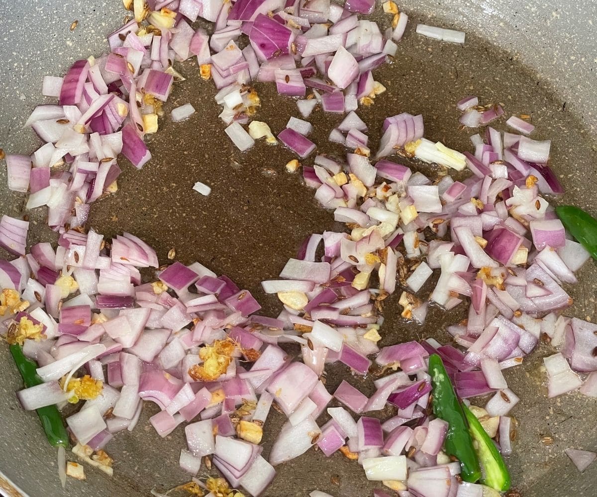 A pan is with onions, chilies and garlic on the stove top.