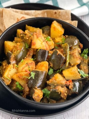 A ceramic bowl of eggplant potato curry is with chapati on the plate.