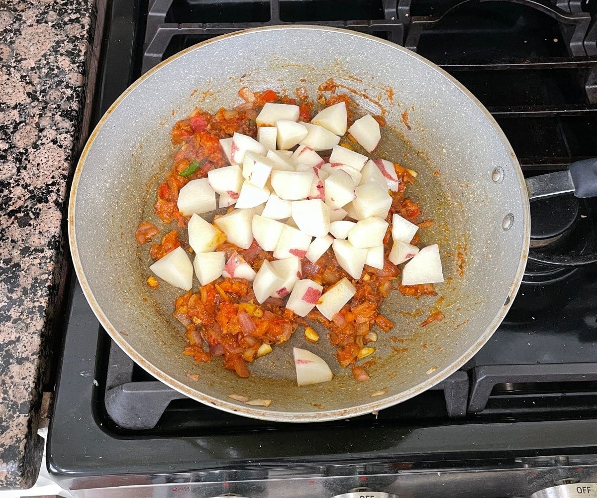 A pan is with aloo baingan masala and chopped potatoes.