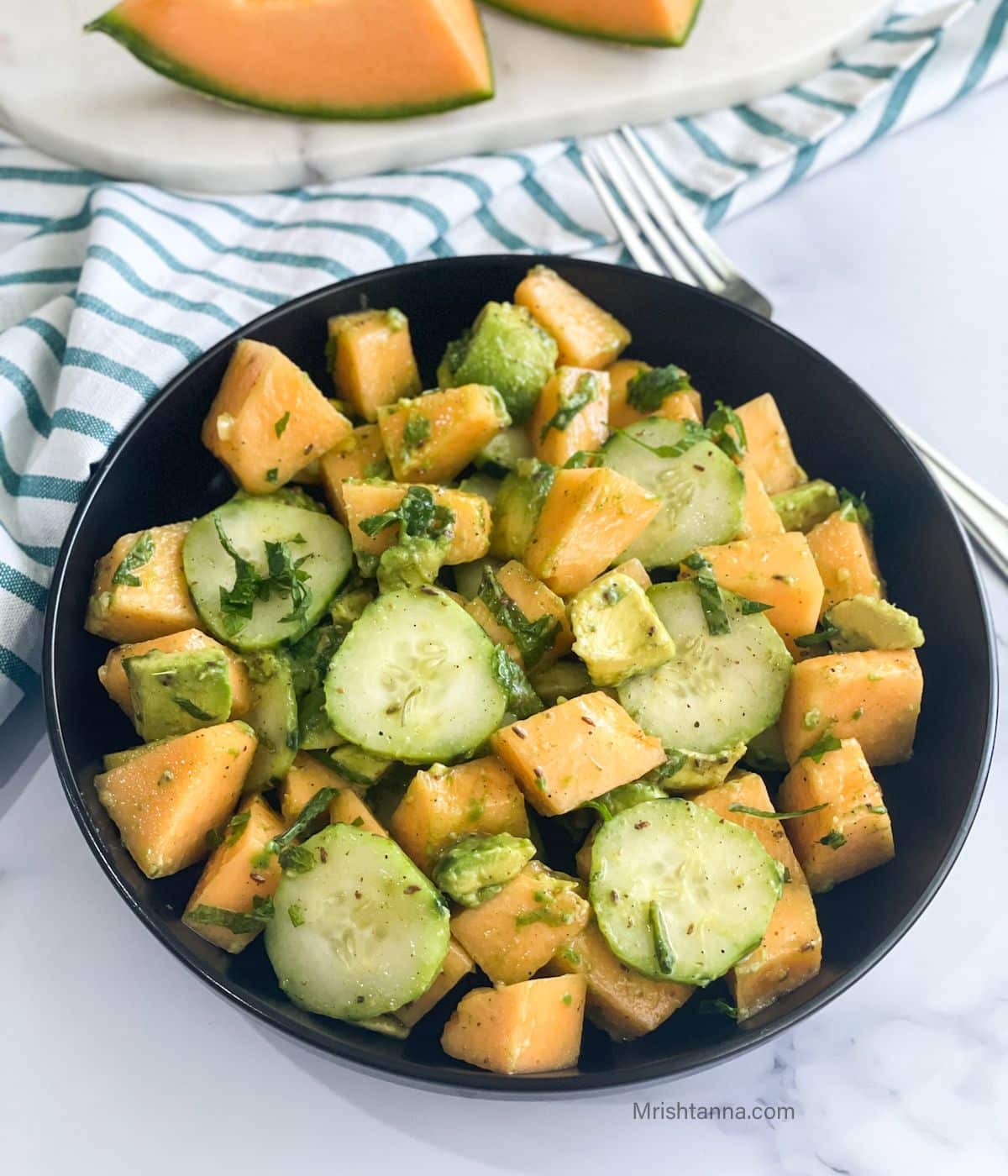 A plate of cantaloupe salad is on the table.