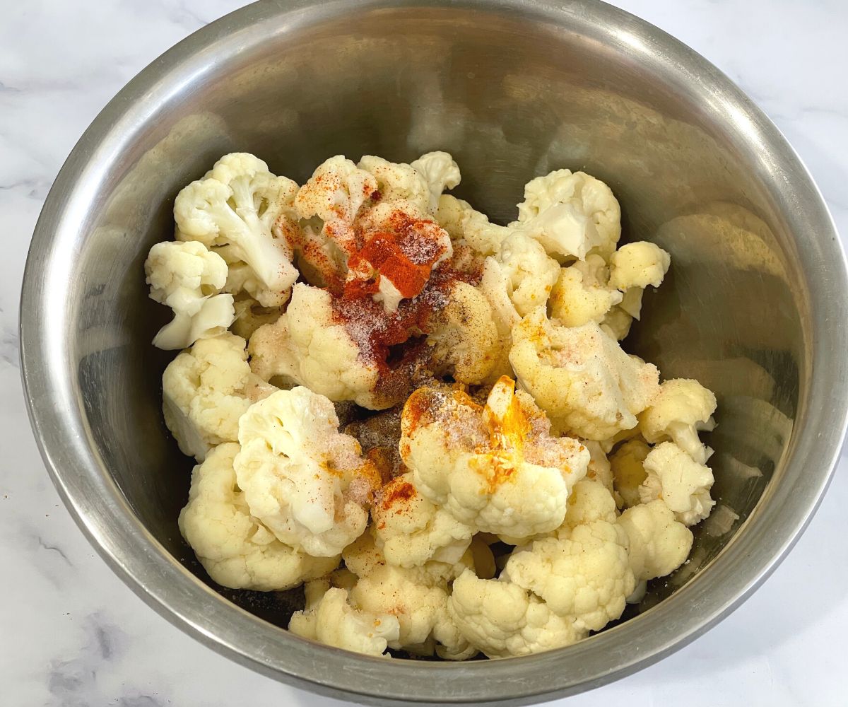 A bowl is with drained cauliflower florets and spices.