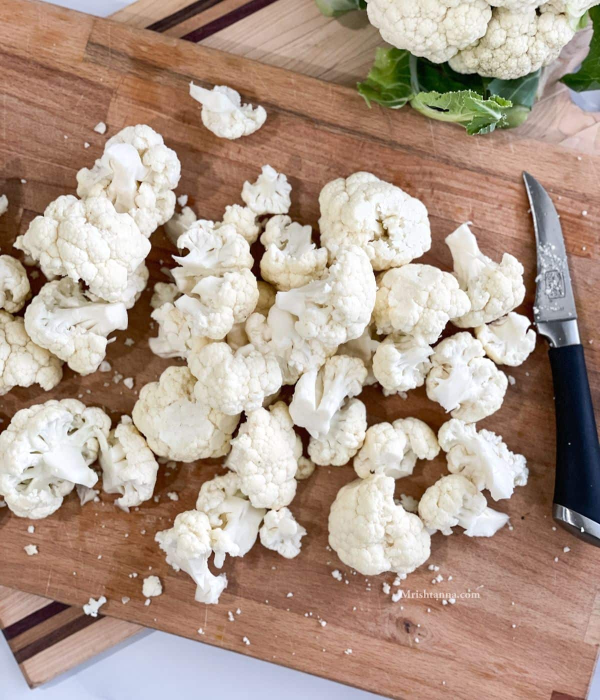 A wooden board is with fresh cauliflower florets and a knife by the side.