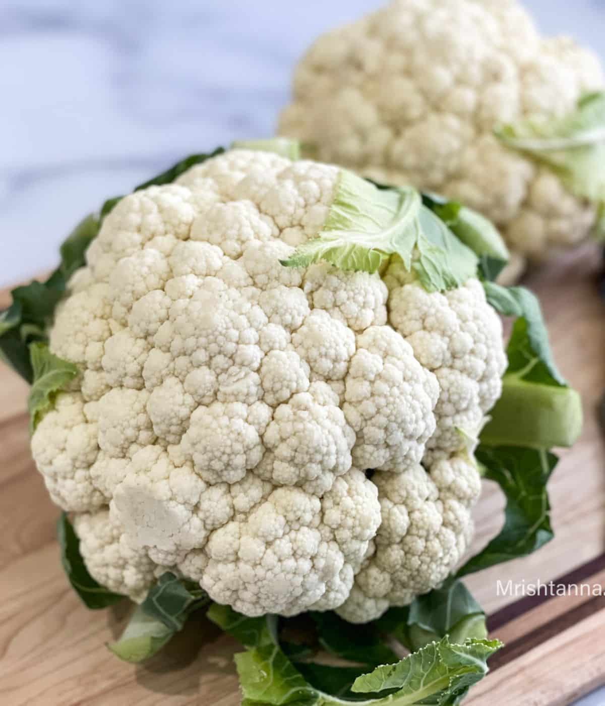 A head of cauliflower is on the wooden board.