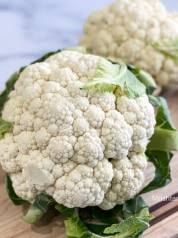 A head of cauliflower is on the cutting board with a knife on the side.