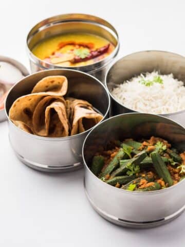 Steel lunch boxes are filled with Indian food.