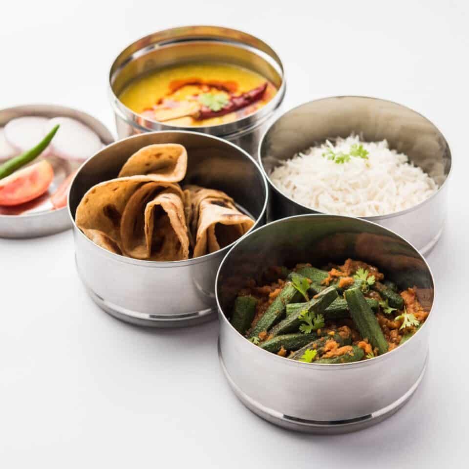 Steel lunch boxes are filled with Indian food.