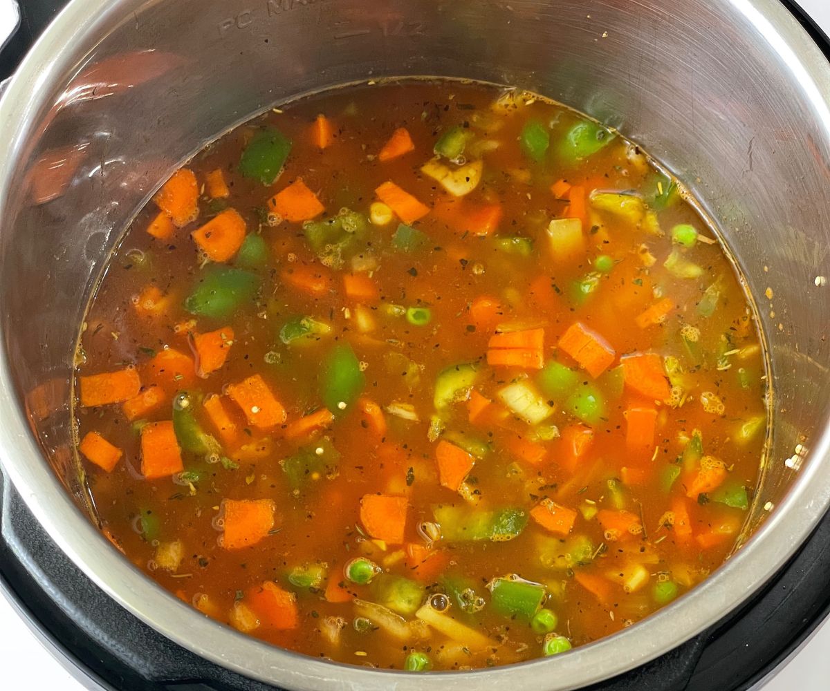 An instant pot is filled with quinoa soup and its on cooking mode.