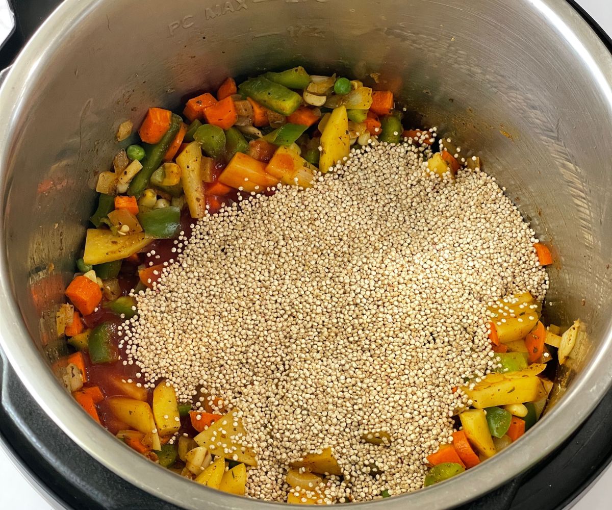 An instant pot is filled with veggies, quinoa and tomato sauce on cooking mode.