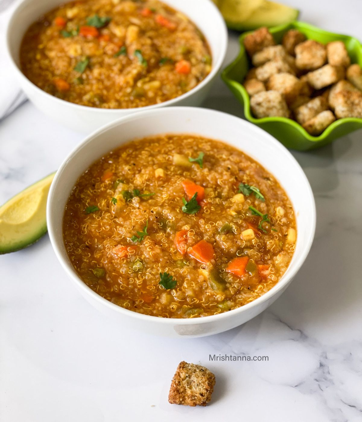 Two bowls of instant pot quinoa vegetable soup are on the table with toppings by the side.