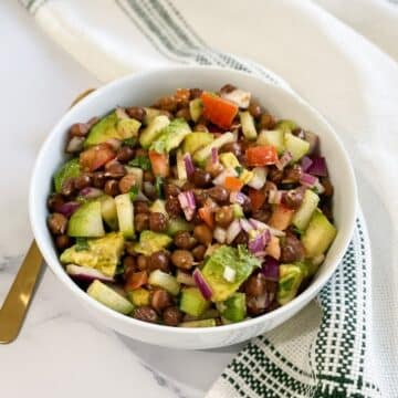 A bowl of kala chana chaat is on the white surface with napkin.