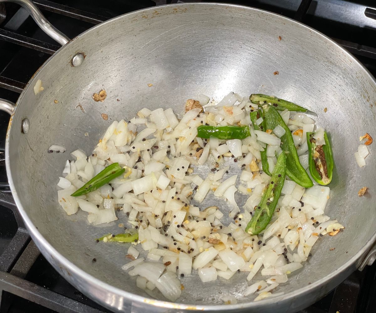 A pan is with spices and chopped onions and chilies over the stove top.