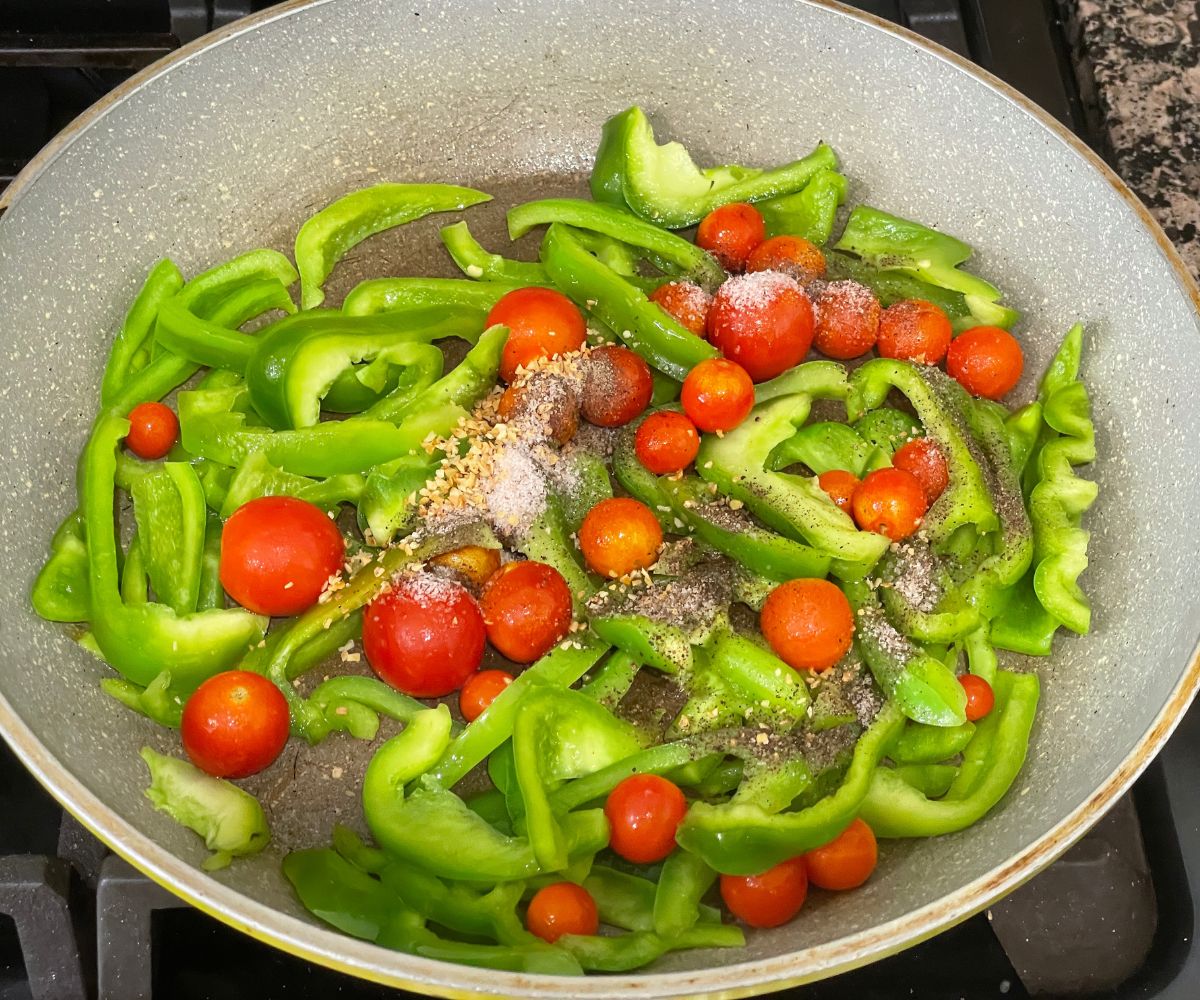 A pan is with cherry tomatoes and bell peppers over the heat.
