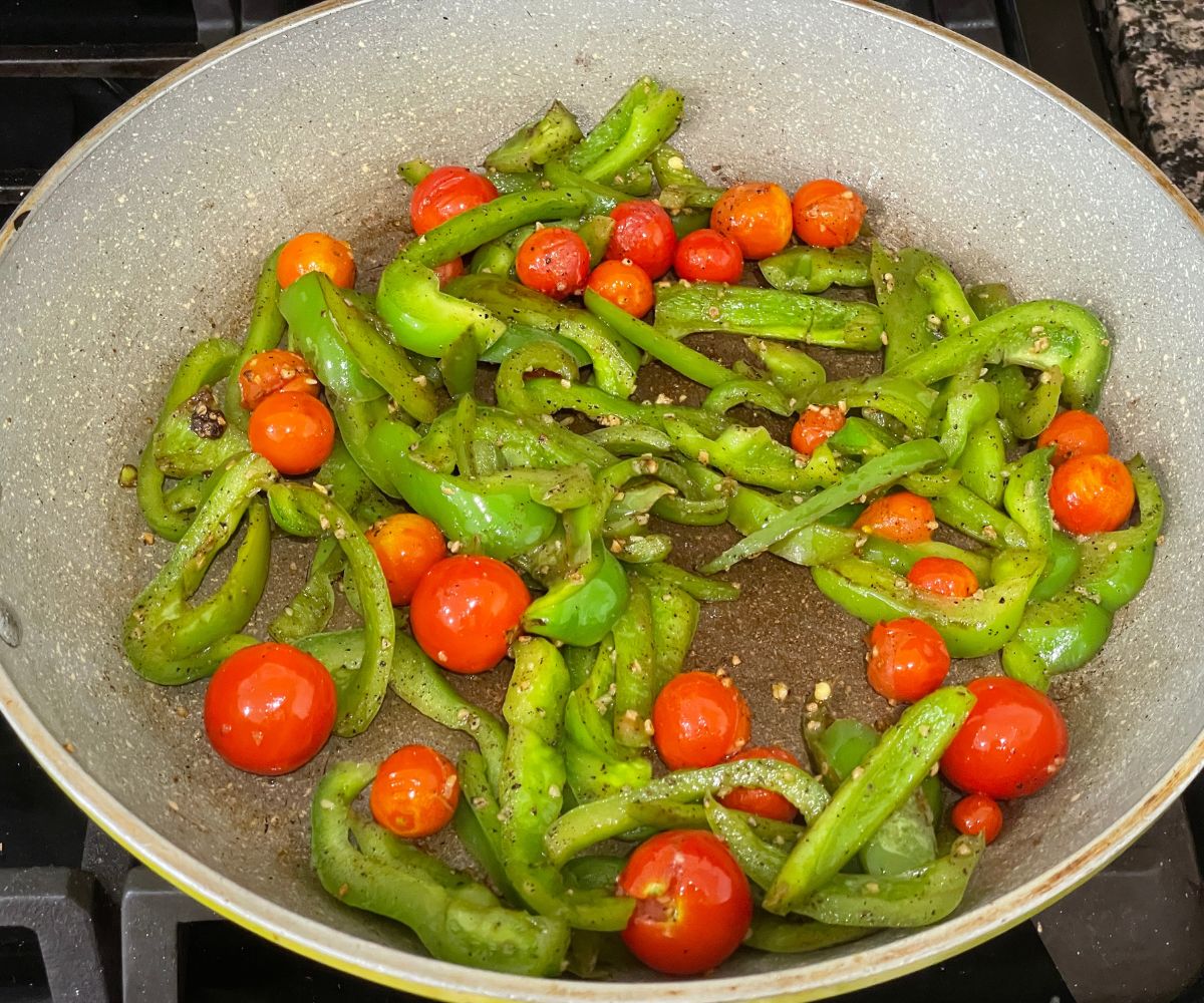 Roasted cheery tomatoes and bell peppers are on the heated pan.