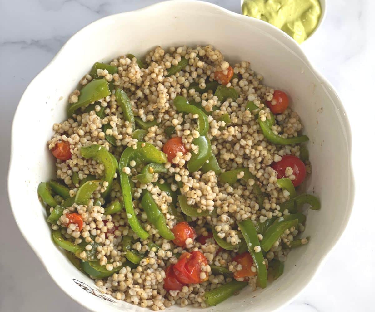 A bowl is with cooked sorghum and roasted vegetables for salad.