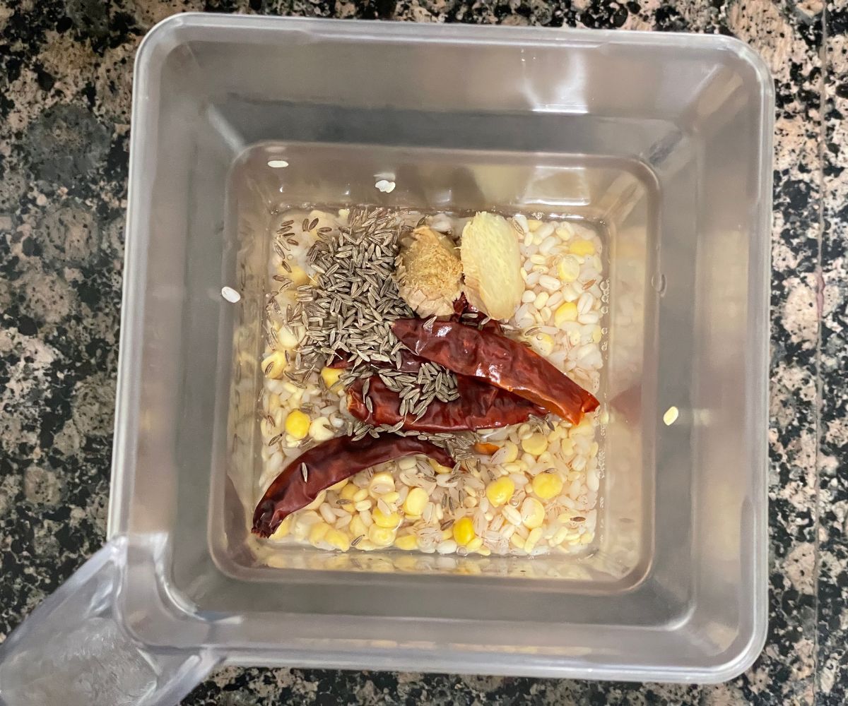 A blender is with soaked rice, lentils and red chilies and placed on the counter top.