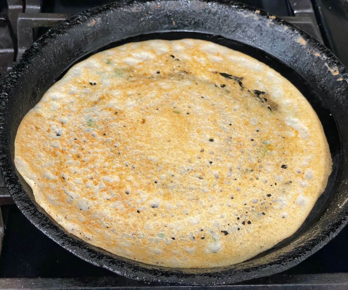 A pan is with filliped adai dosa over the heat.