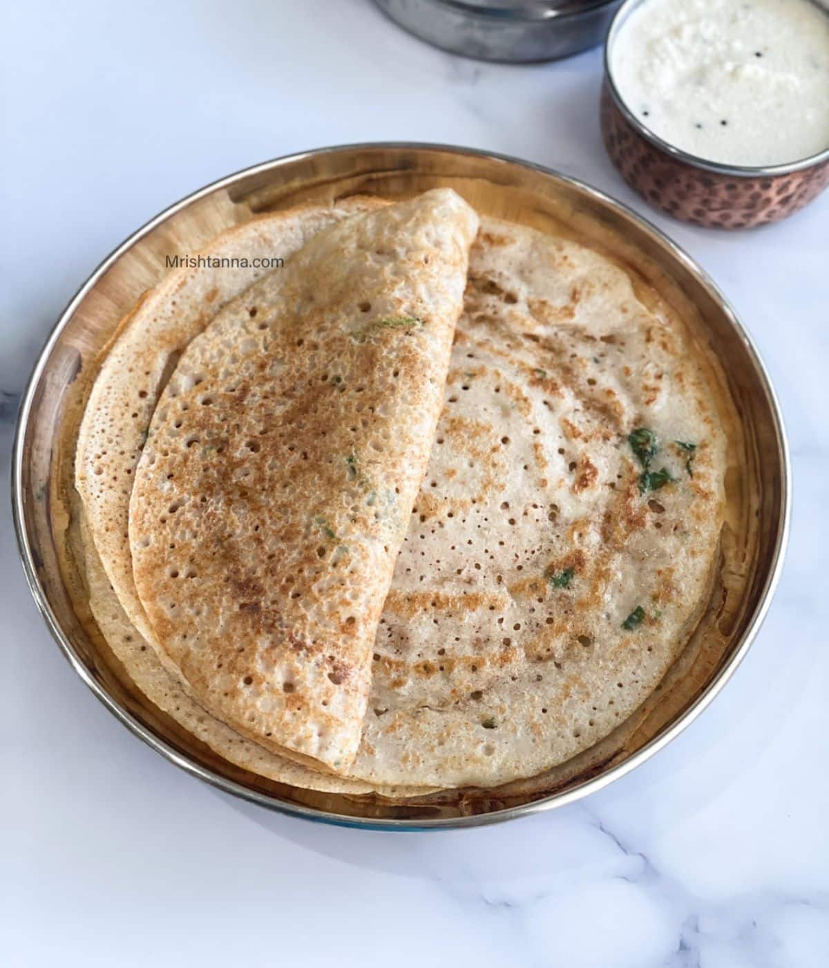 A plate is with adai dosa and a bowl of chutney is on the side.