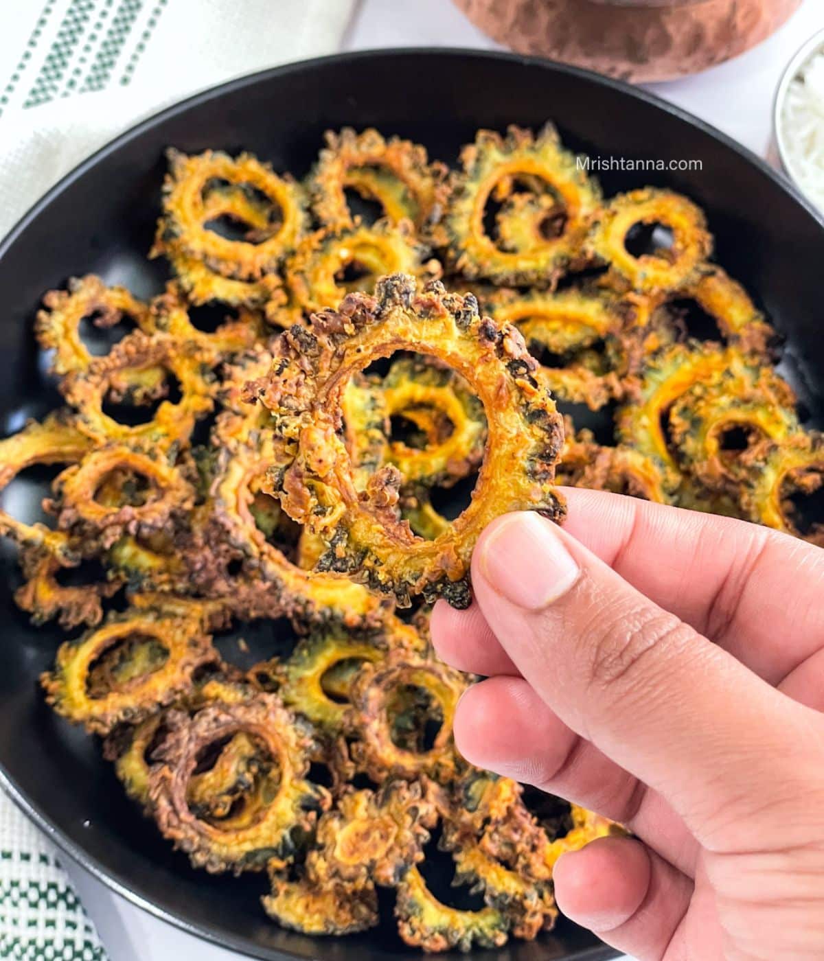 A hand is holding air fried bitter gourd chips.