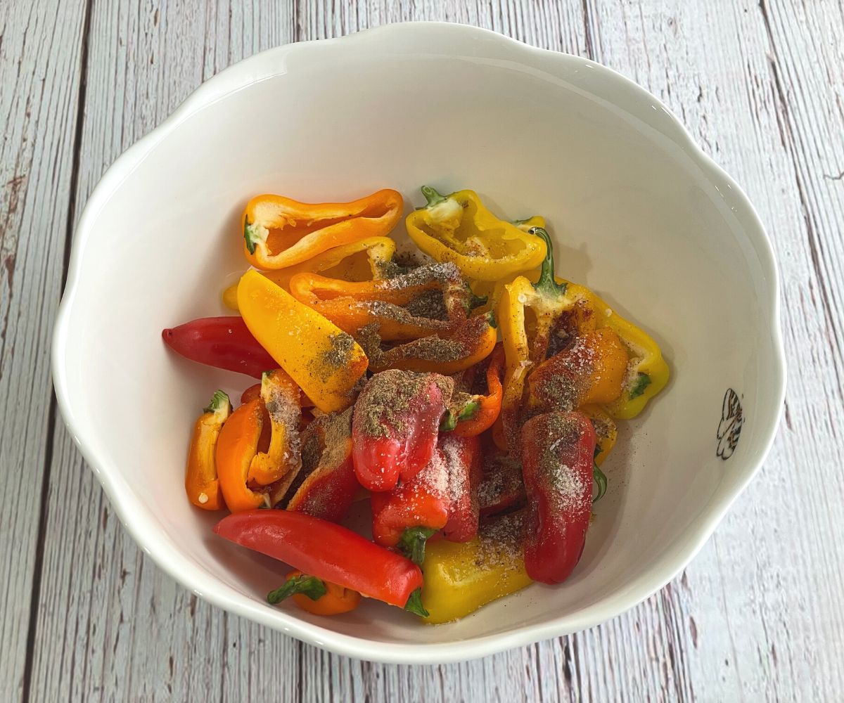 A bowl is with sliced mini peppers, seasonings and salt.