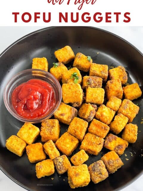 A plate of air fryer tofu nuggets are on the table with tomato ketchup.