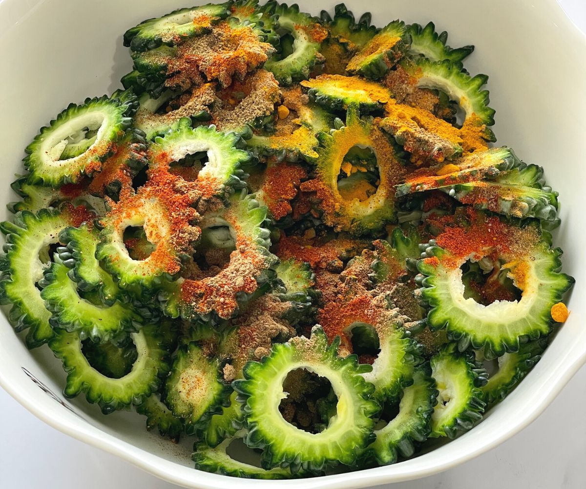 A bowl is with sliced bitter gourd, spices and salt on the table.