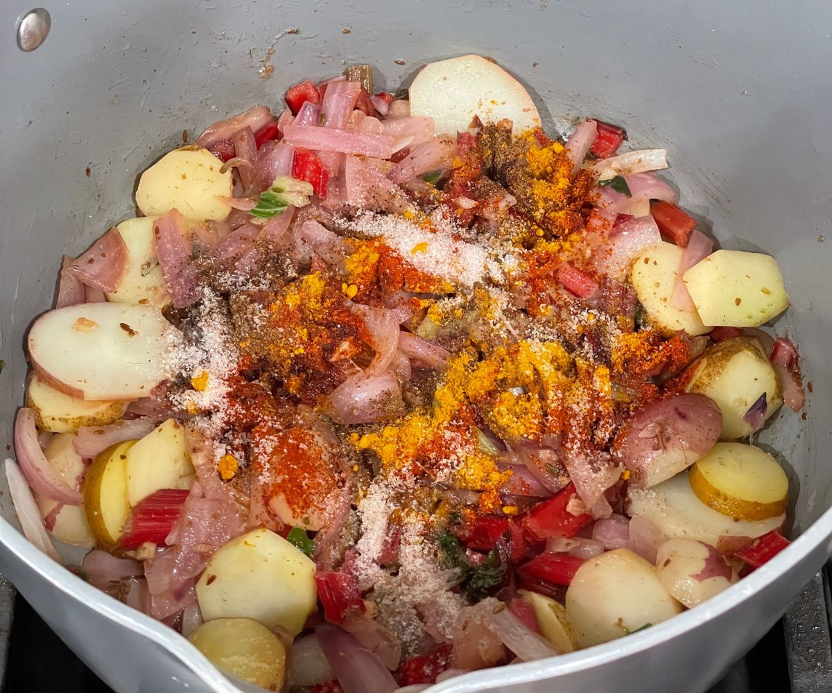 A pot is with swiss chard stalks, potatoes and onions over the heat.