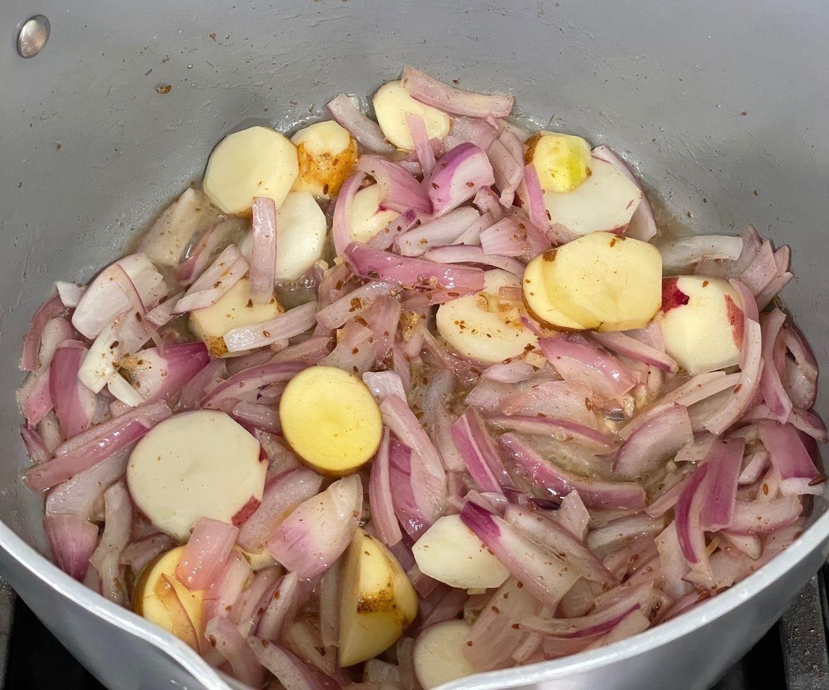 A non stick pot is with spices, onions, chopped garlic and ginger over the heat.