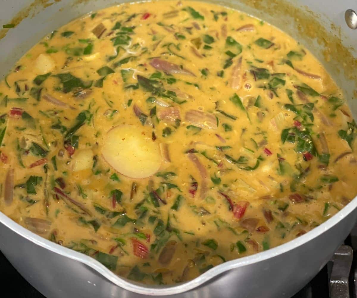 A pot is with swiss chard curry with potatoes and lentils over the stove top.