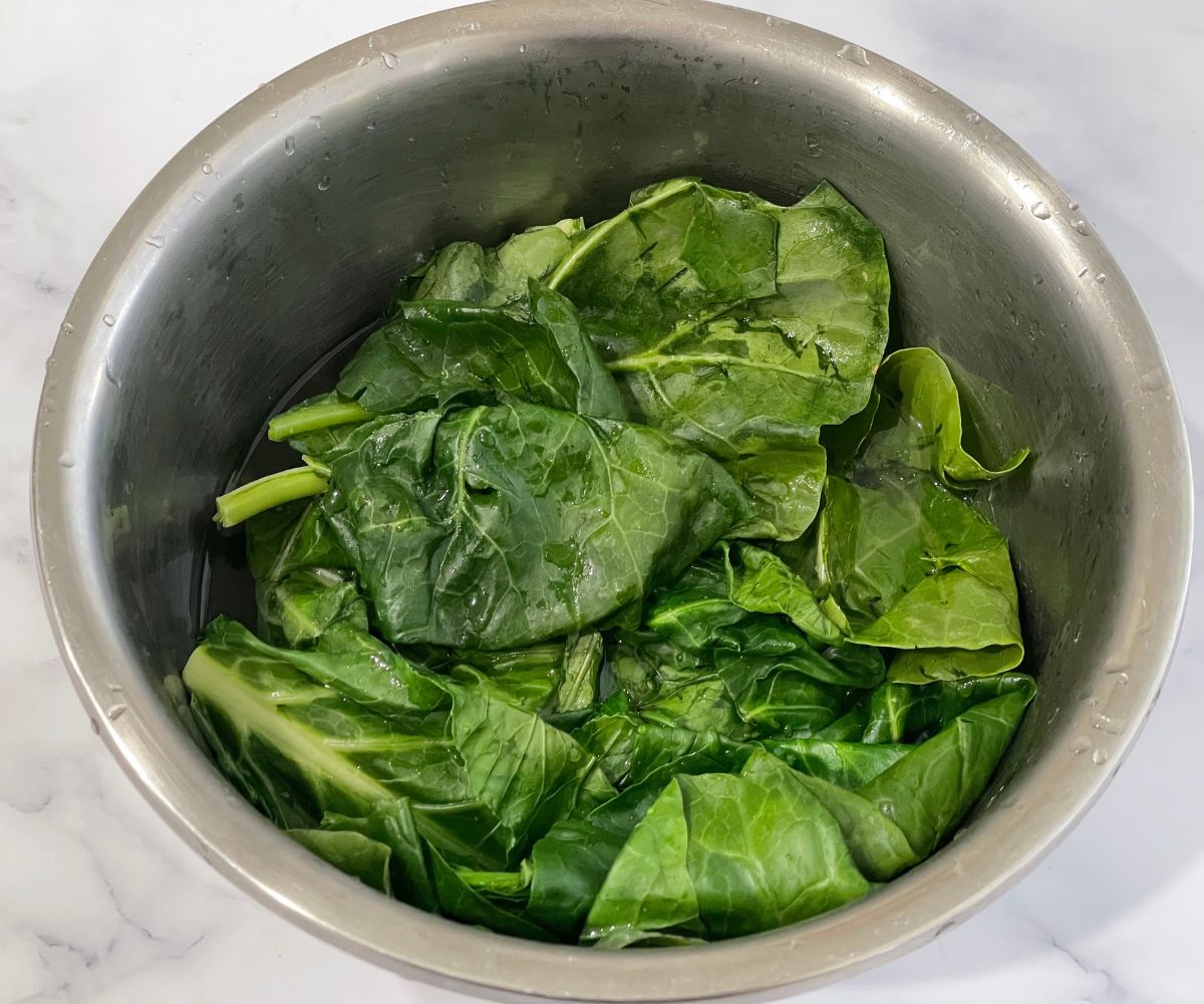 A bowl is with hot water and collard greens.