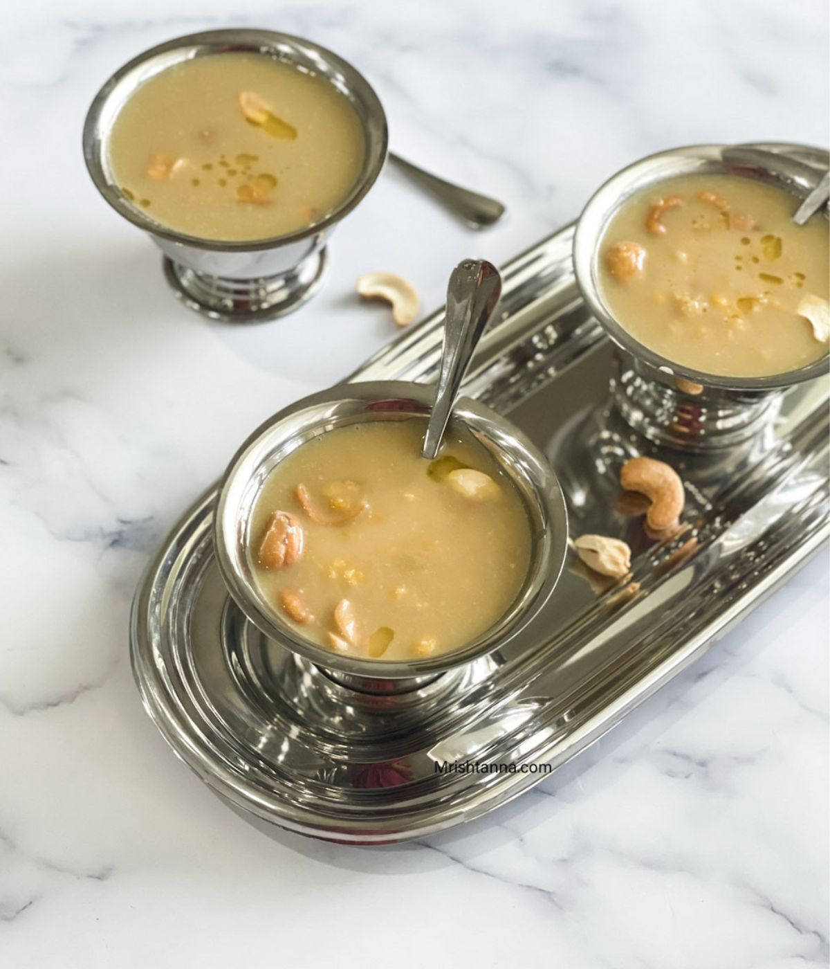 Three stainless steel bowls are with chana dal payasam and topped with roasted cashews.