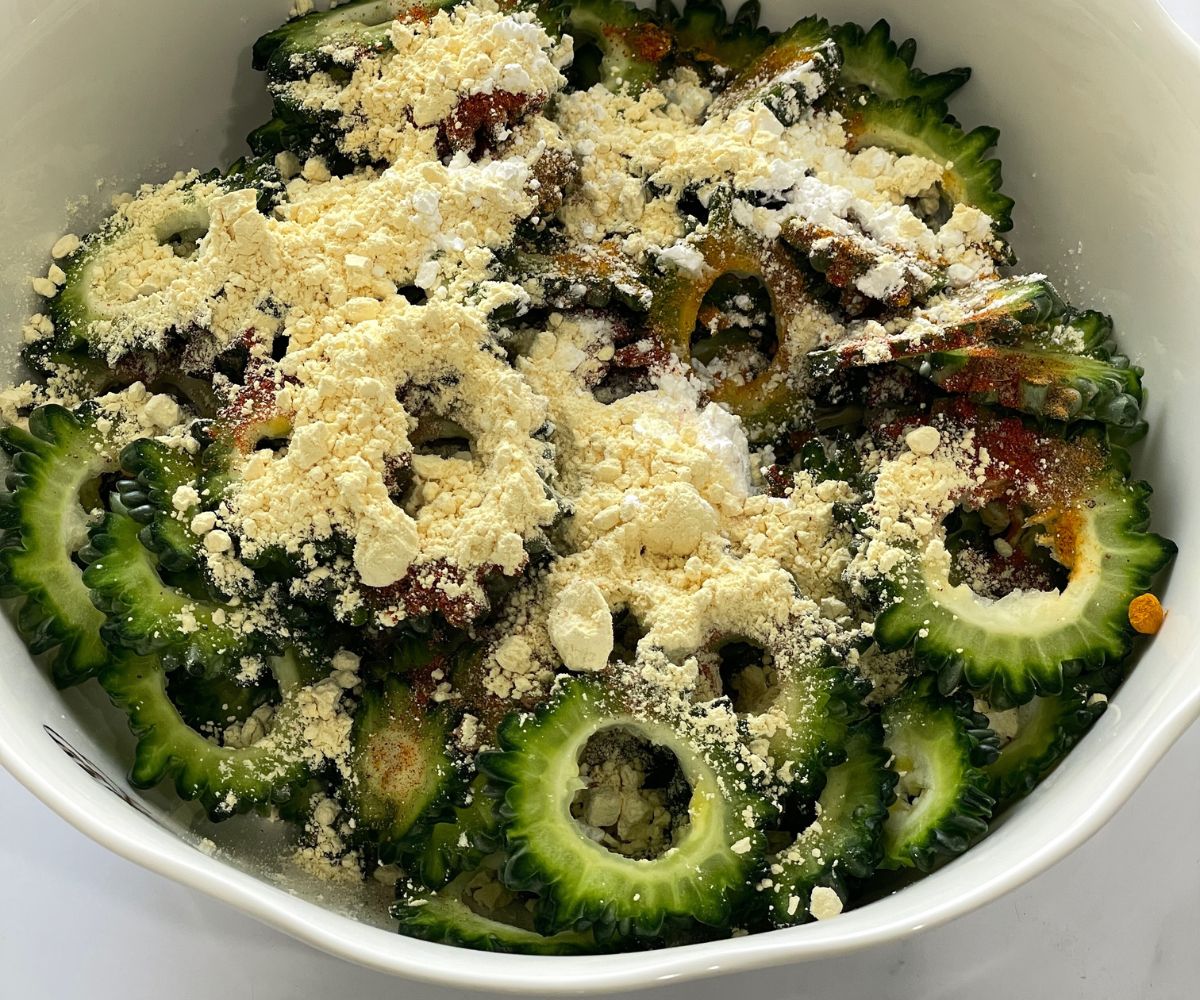 A bowl of bitter gourd slices are coated with flours and spices.