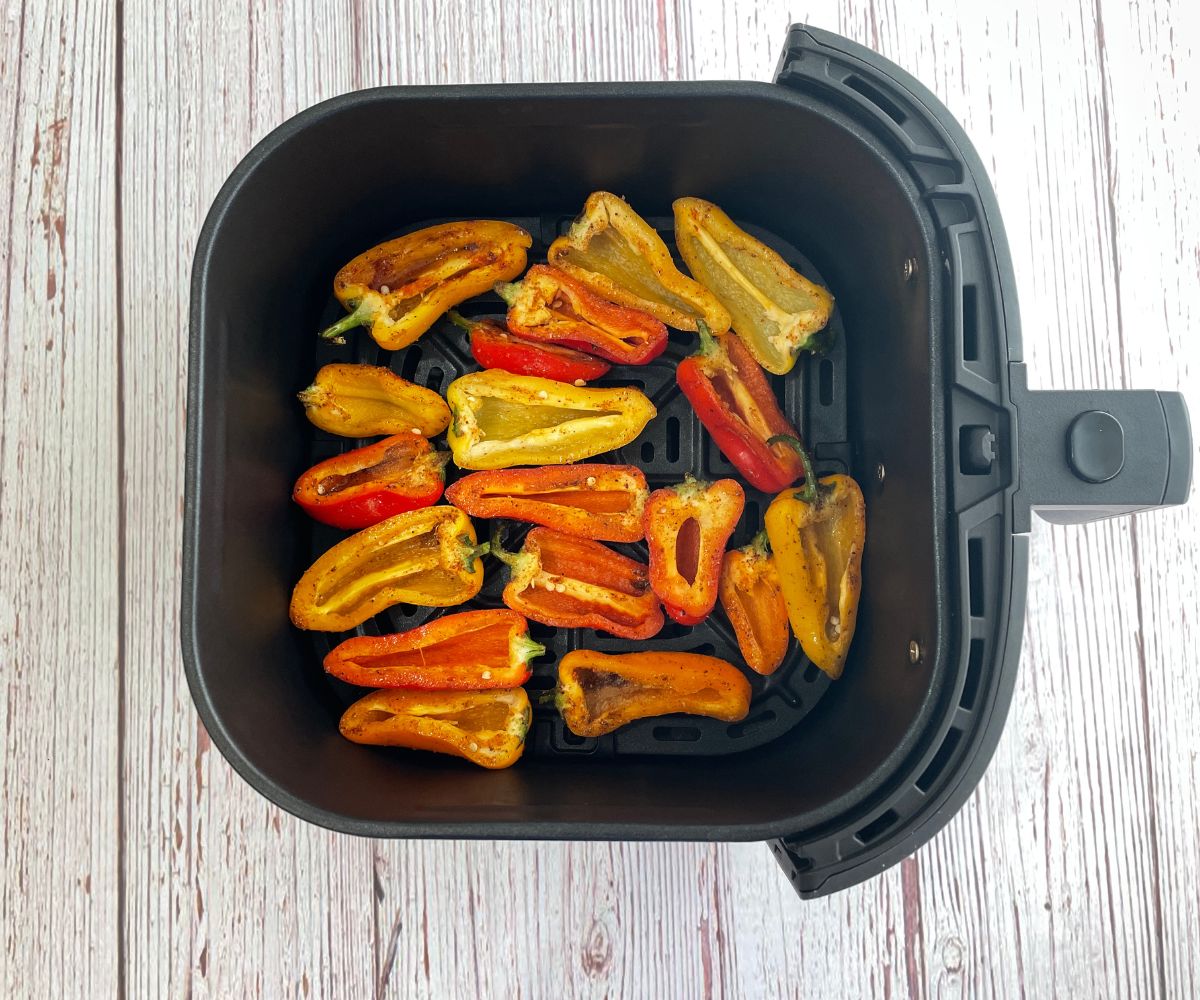 The air fryer basket is filled with seasoned peppers.