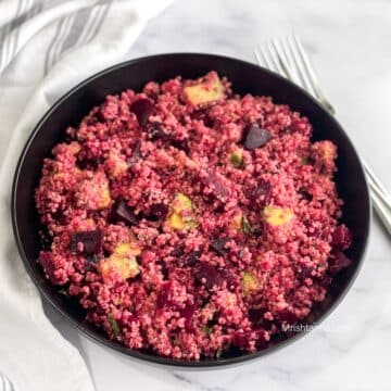 A plate of quinoa and beets salad is on the table with a fork.