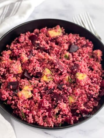 A plate of quinoa and beets salad is on the table with a fork.