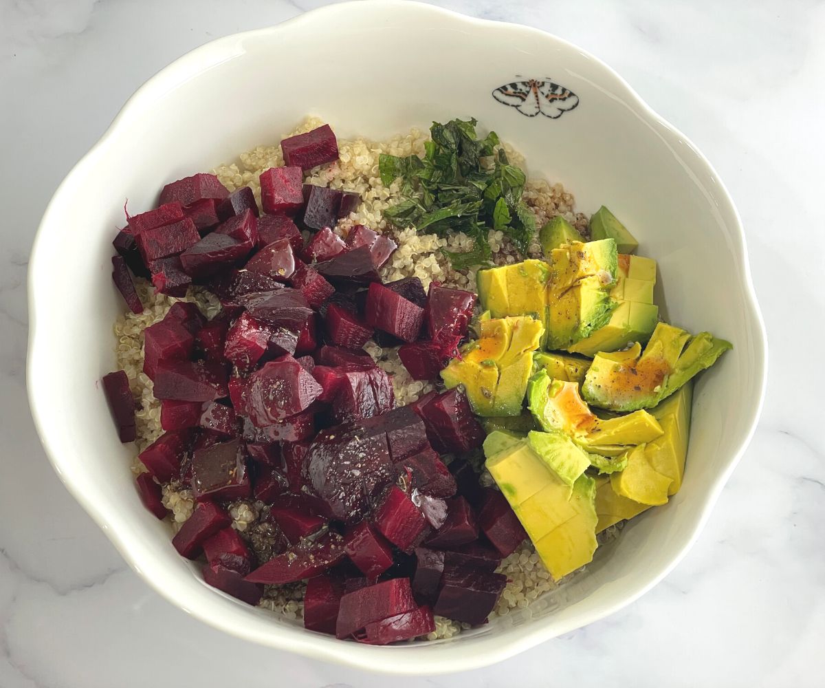 A large bowl is with cooked quinoa, beets and avocado.
