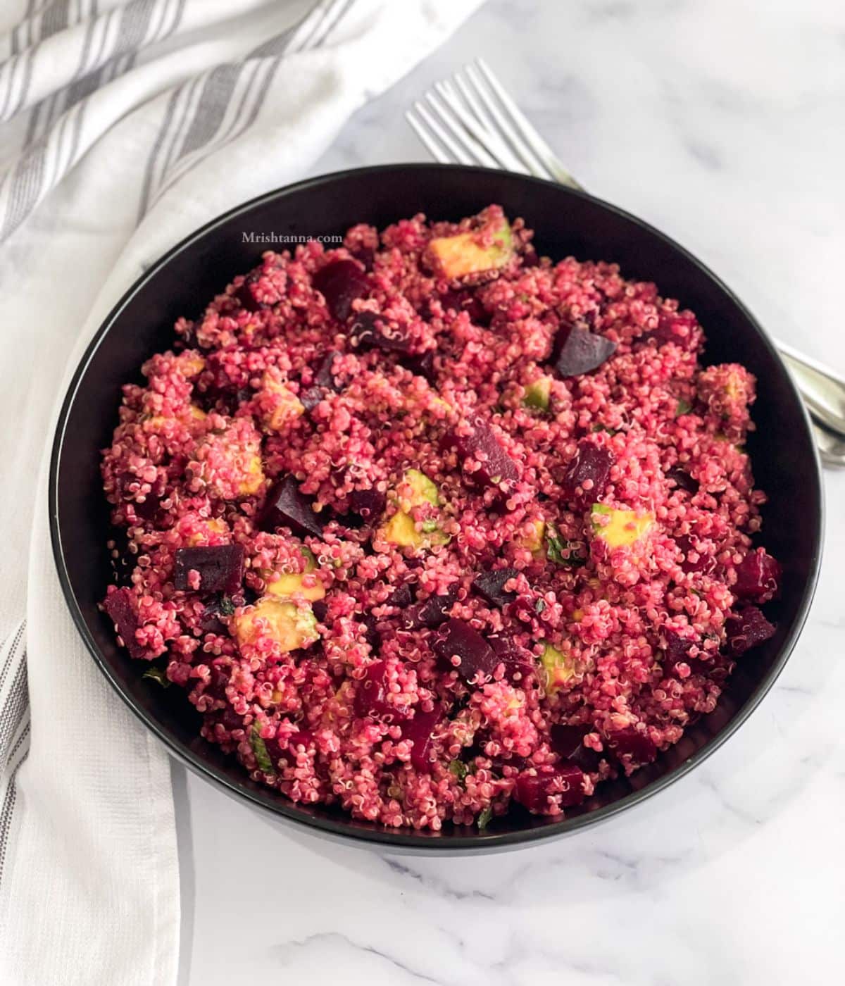 A plate of quinoa salad with beets is on the table with a fork on the side.