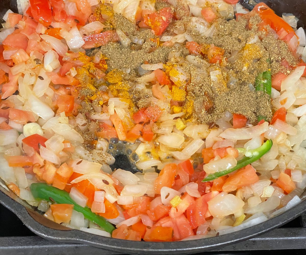 A skillet is with onions, chopped tomatoes and spices over the heat.