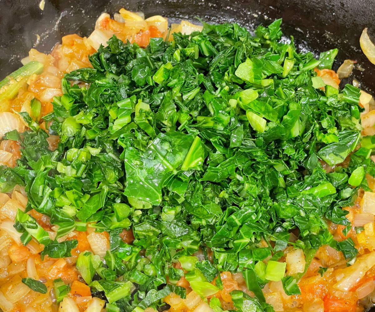 A large skillet is with spices and chopped collared greens over the heat.