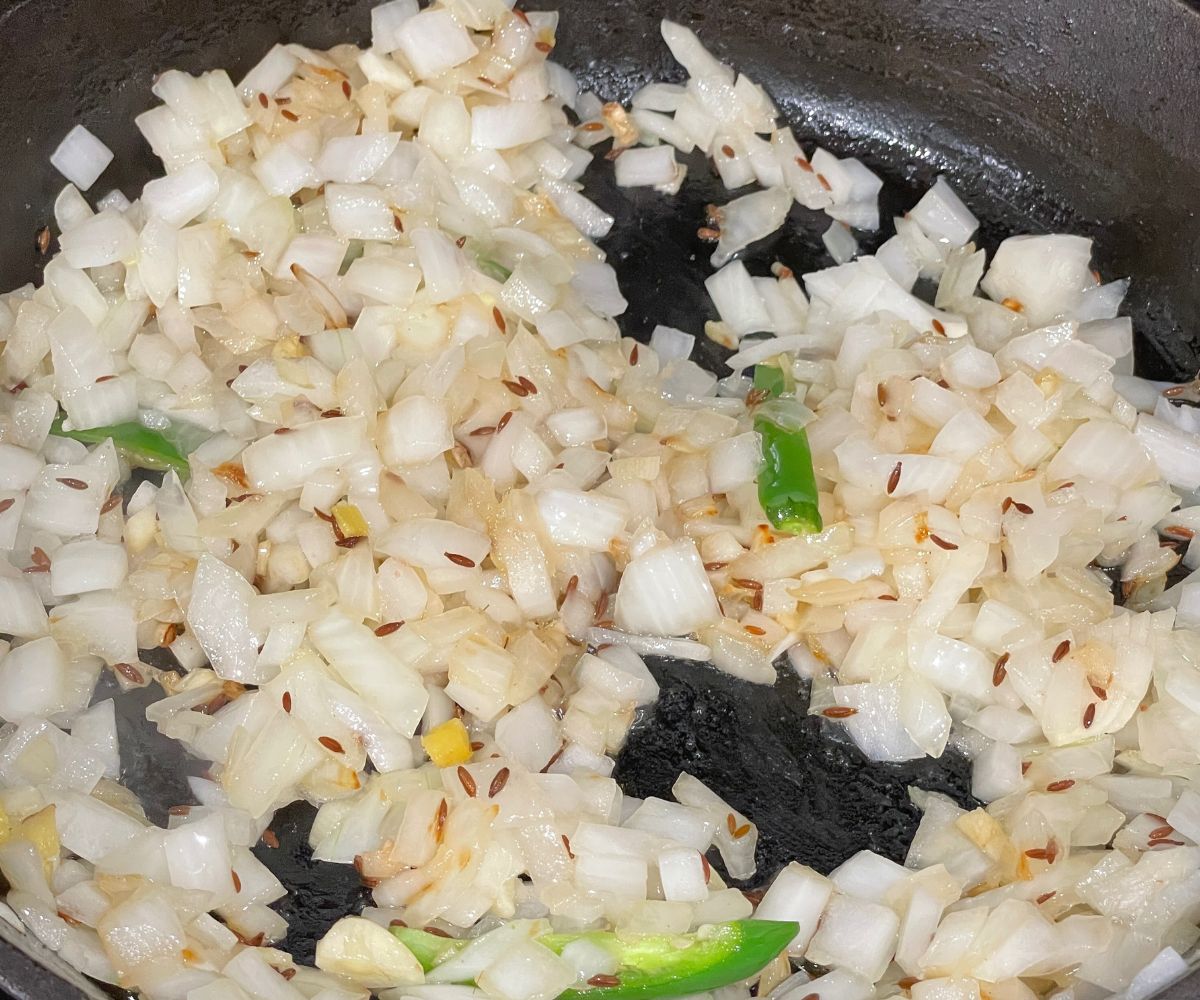 A cast iron skillet is with ginger, garlic and onions over the heat.