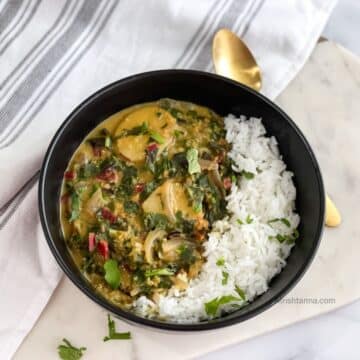 A bowl of Swiss chard curry and rice is on the table with a spoon and cloth napkin by the side.