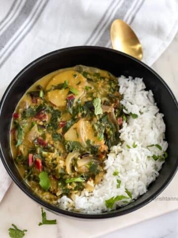 A bowl of Swiss chard curry and rice is on the table with a spoon and cloth napkin by the side.