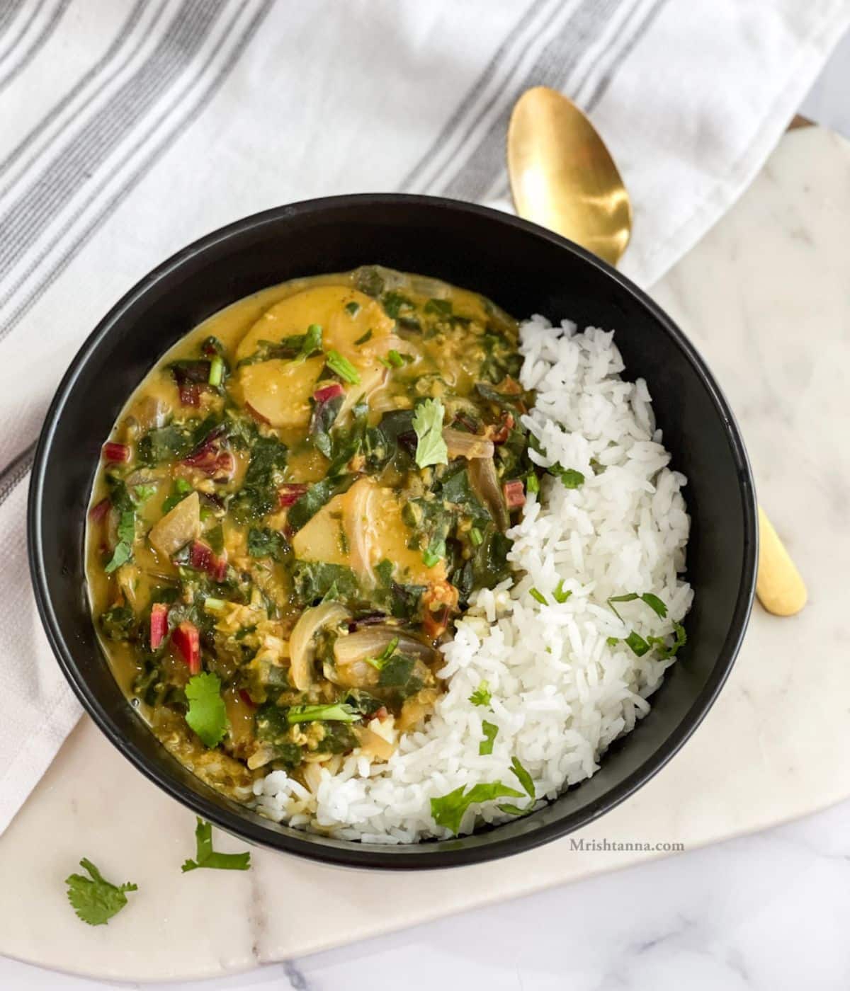 Head shot of bowl with Swiss chard curry and a golden spoon by the side and napkin under the bowl.