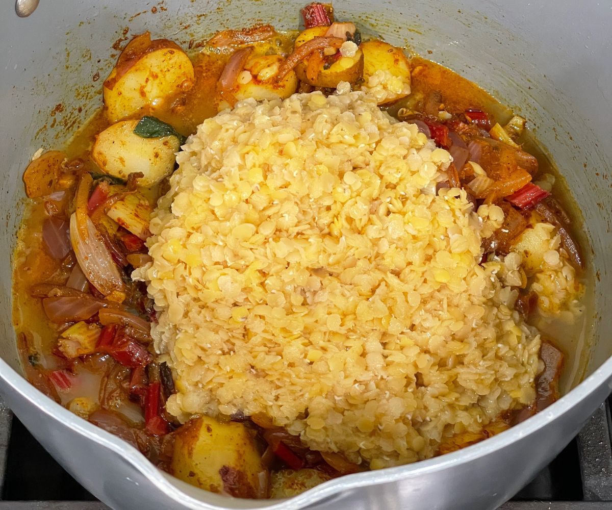 A pot is with lentils, potatoes, spices and swiss chard for curry over the heat.