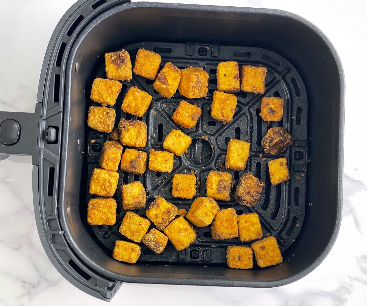 Air fryer basket is with fried tofu nuggets.