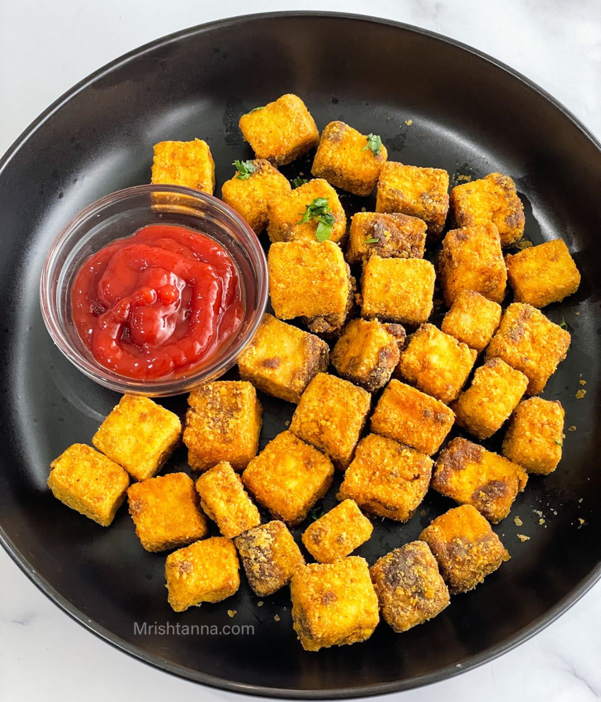 A plate of air fryer tofu nuggets and a bowl with ketchup is on the table.