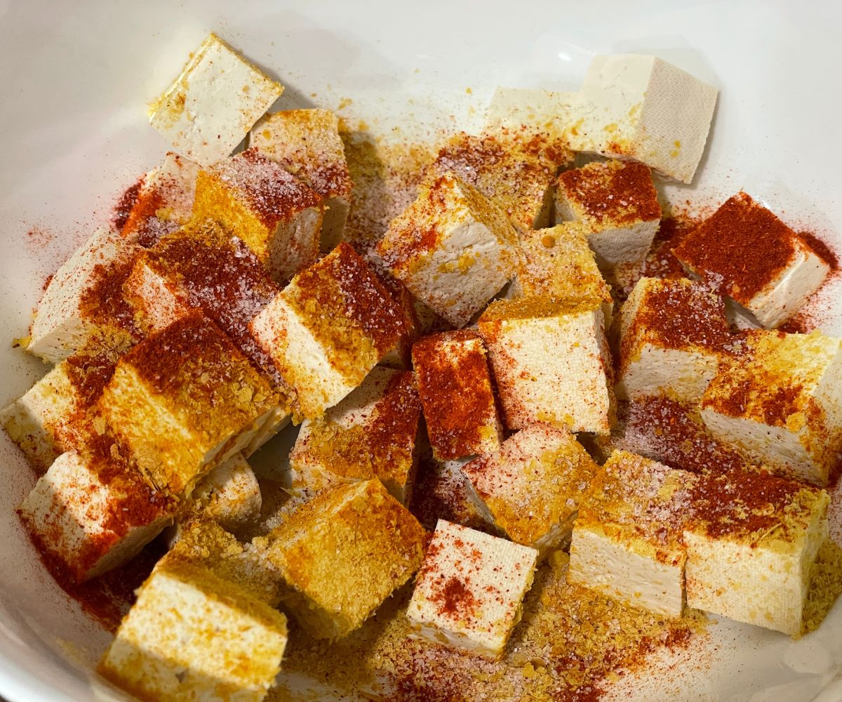 A bowl is with cubed tofu and spices.