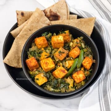 a bowl of vegan saag paneer with tofu is on the plate with chapati.