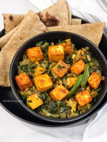 a bowl of vegan saag paneer with tofu is on the plate with chapati.