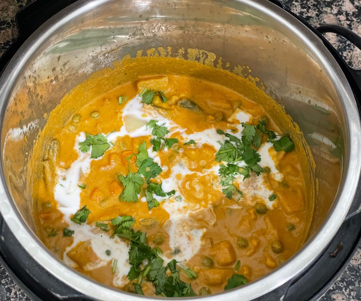 An instant pot is with vegetable korma and topped with cilantro and coconut milk.