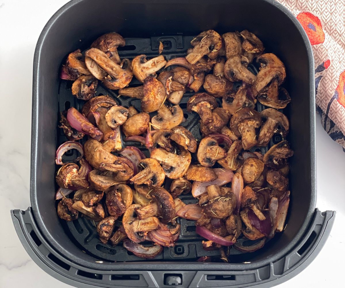 Air fryer basket is with fried mushrooms and onions.